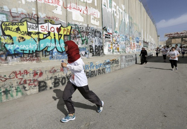 Participants run past Israeli barrier during Palestine Marathon in the West Bank town of Bethlehem